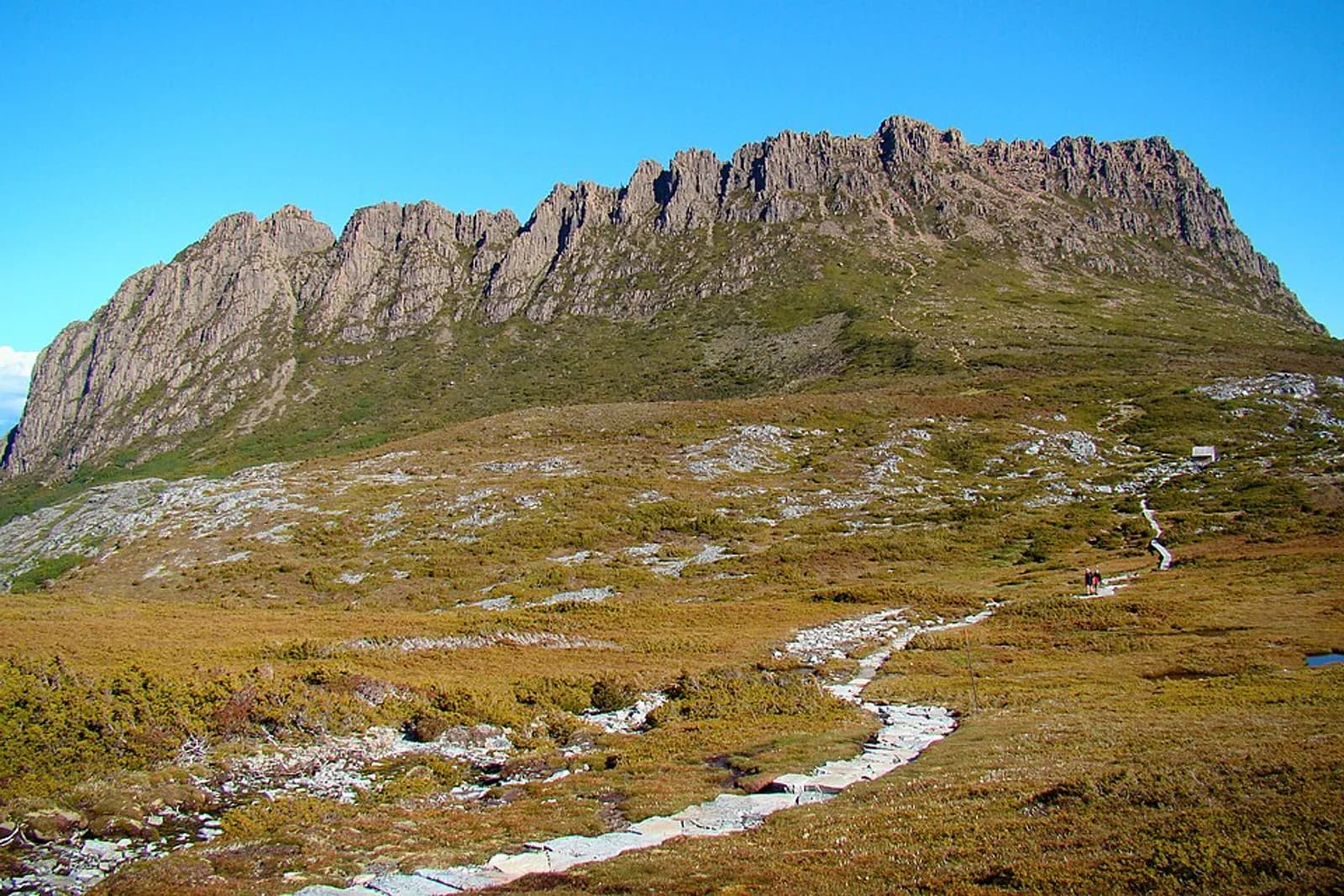 The Overland Track winding past Cradle Mountain on a midsummer day. The cabin seen in the right centre is Kitchen Hut, only for emergency use.
