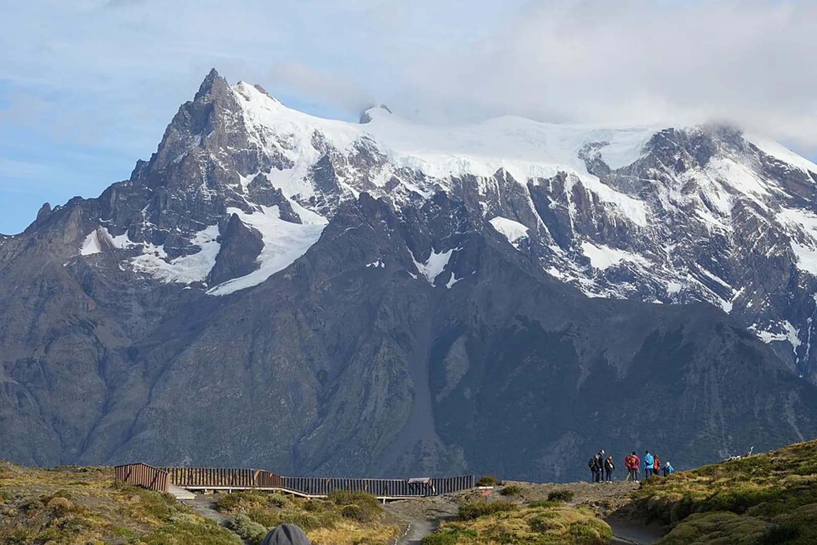 View of Cerro Paine Grande and its glaciers from Mirador Salto Grande in Torres del Paine National Park, Patagonia, Chile. A group of hikers can be seen on the trail in the foreground.